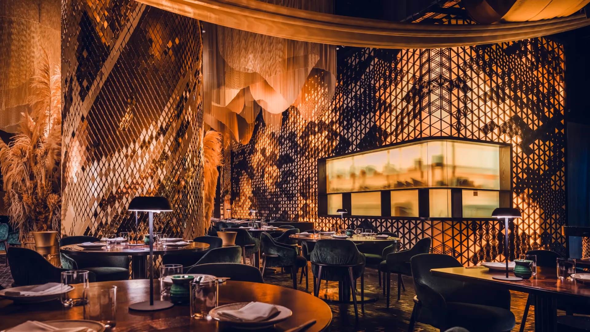 Main dining room at Strawfire, Emirates Palace Abu Dhabi, with a back-illuminated Kumiko screen, a slot view into the kitchen and set tables
