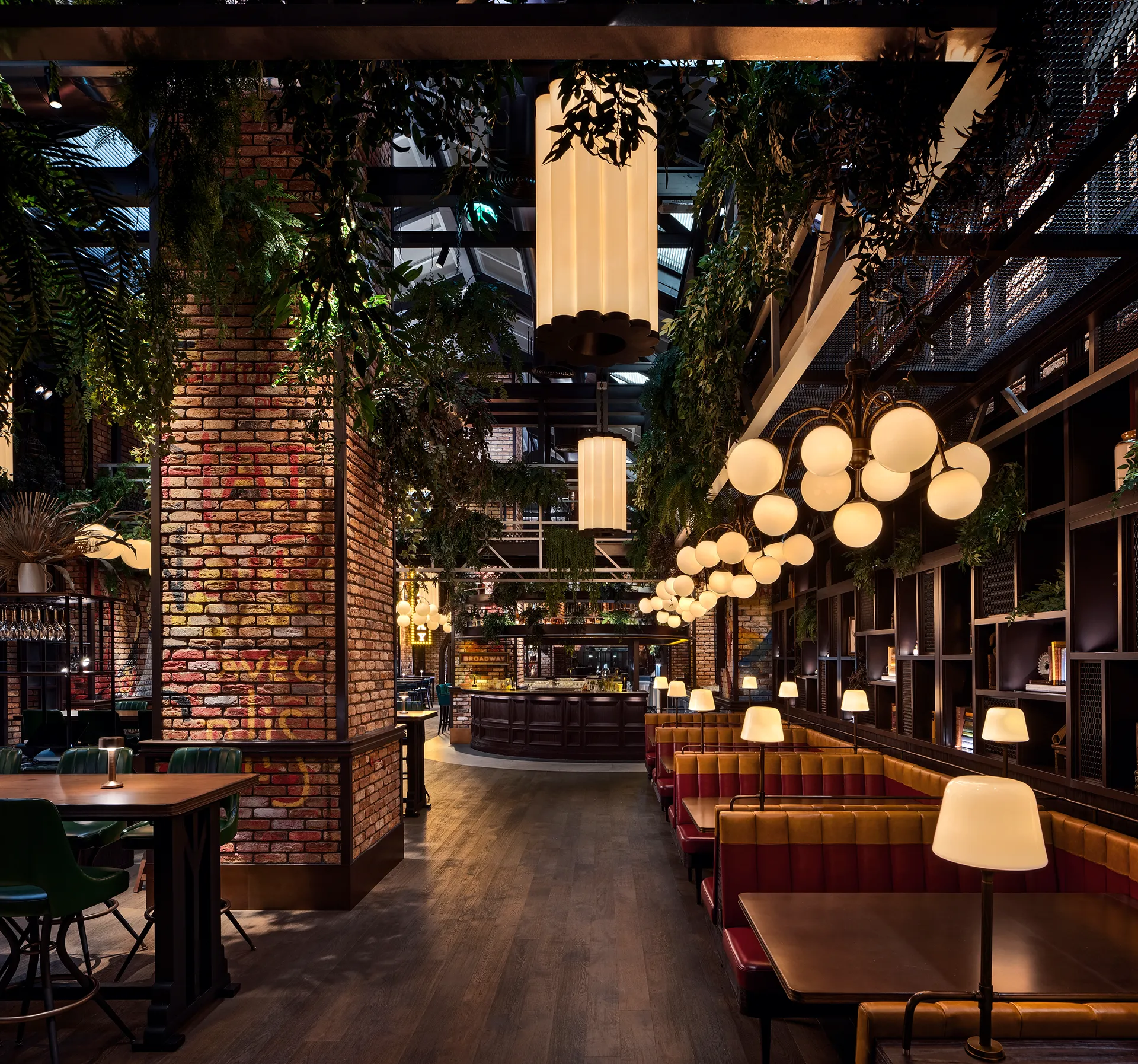 Booth seating at Broadway, Emirates Palace Abu Dhabi, with red leather banquettes, globe pendant clusters, exposed brick columns and hanging greenery