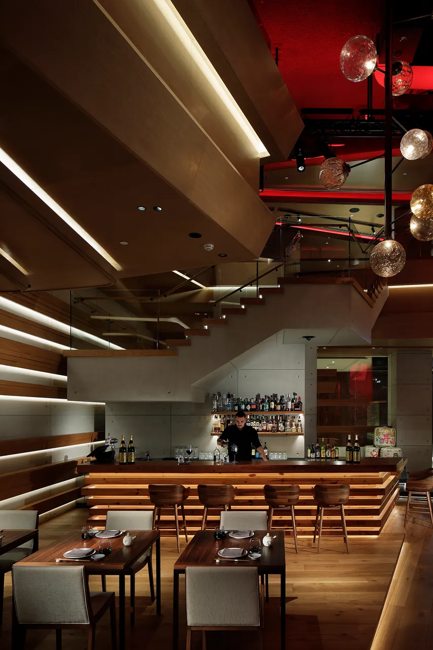 Lounge bar at Netsu, Mandarin Oriental Jumeira Dubai, with a lit timber bar beneath the staircase to the upper level and hand-blown glass globe pendants