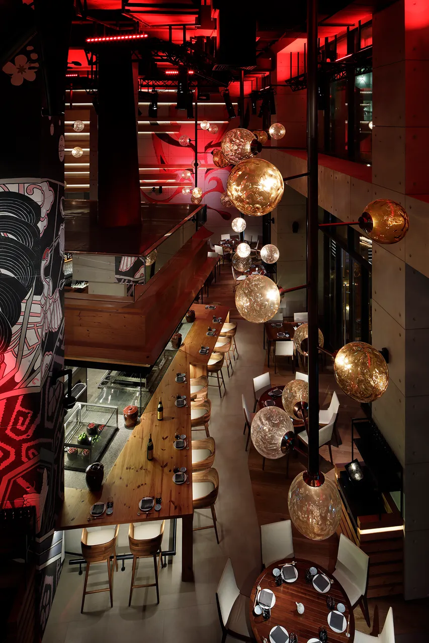 View from the level 2 lounge down to the main dining area at Netsu, Mandarin Oriental Jumeira Dubai, through suspended hand-blown glass globe lamps