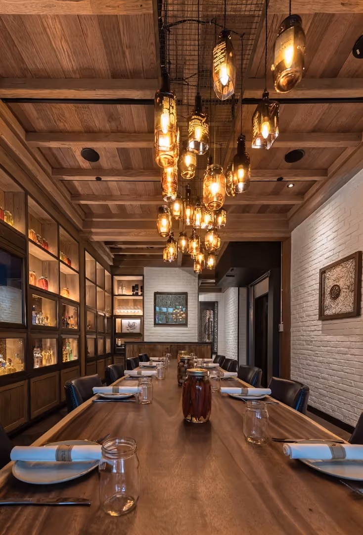 Yardbird private dining room with a long reclaimed wood table, a chandelier of repurposed glass bottles and whitewashed brick walls