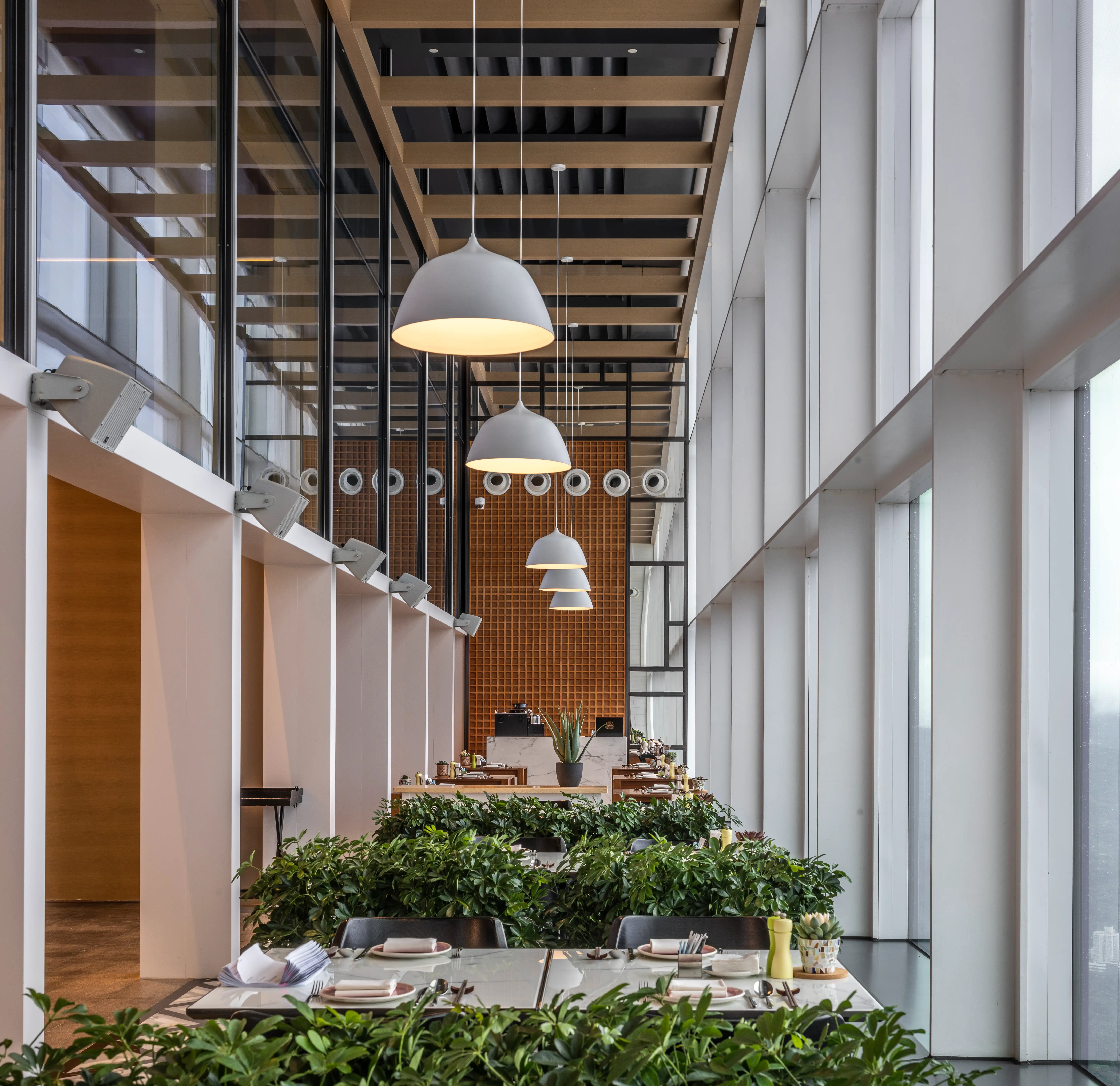 Bazaar balcony seating beneath a double height glass wall, with white pendant lamps, planters and a brick feature wall