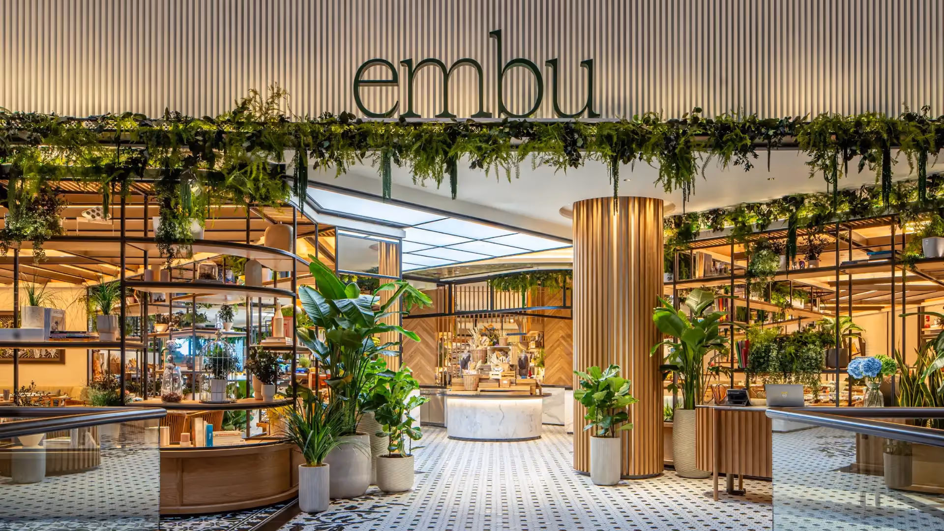 Facade of embu at Mandarin Oriental, Singapore, with greenery-draped signage, glass balustrades and Peranakan black and white floor tiles