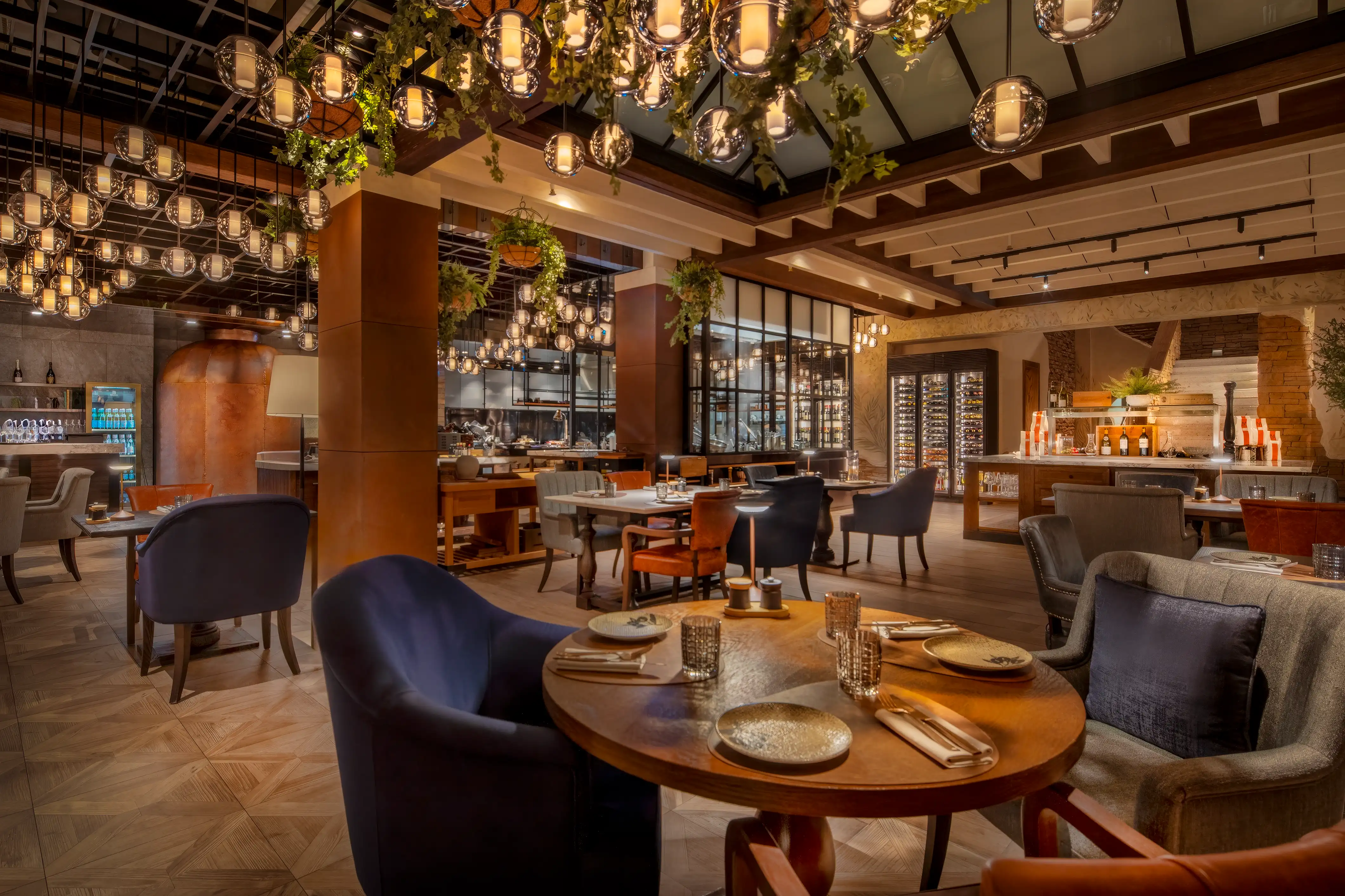 Dining room with dark timber beams, wood-topped tables, blue velvet armchairs and hanging greenery at Essenza, Mandarin Oriental, Muscat