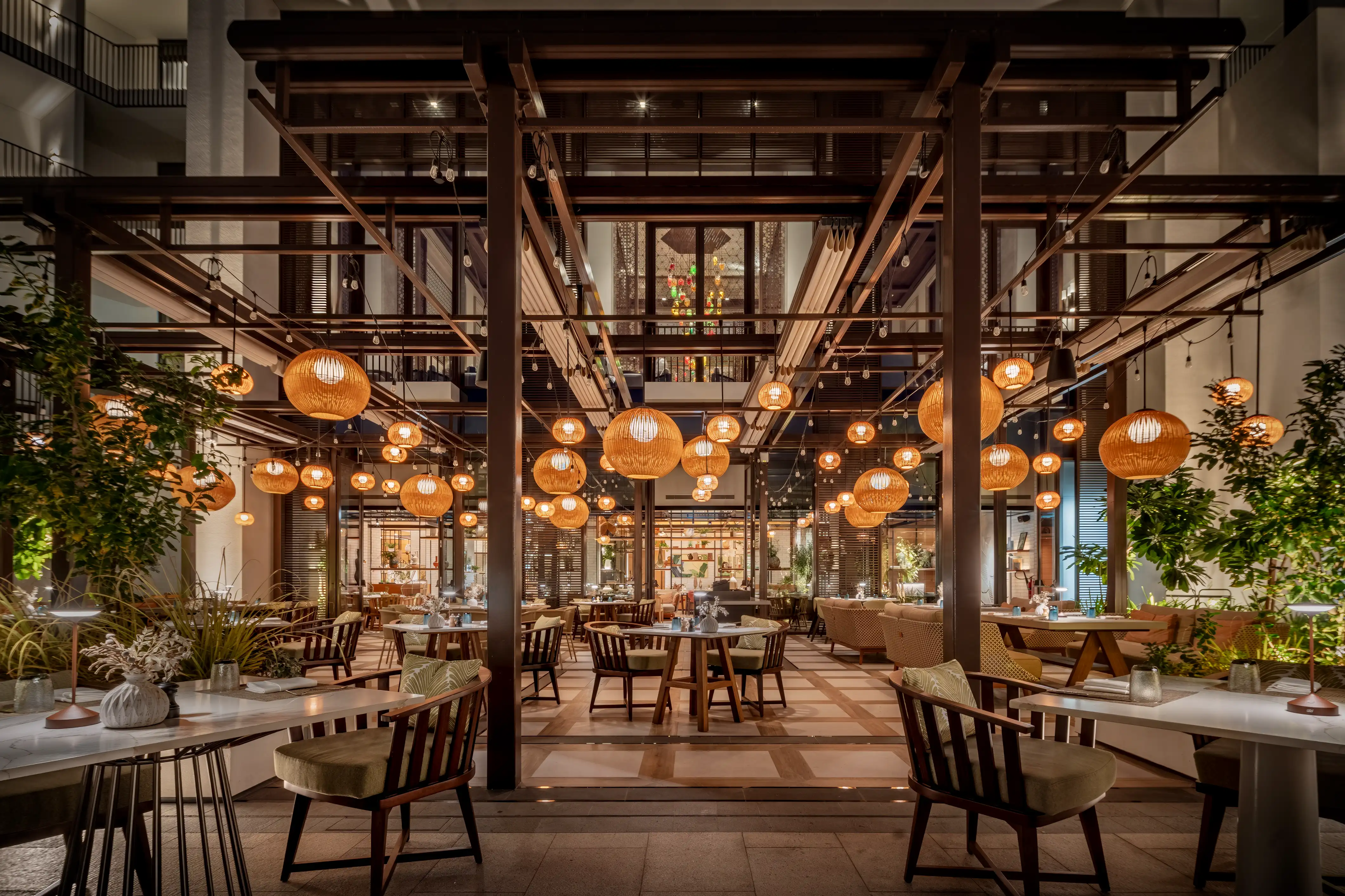 Courtyard dining under exposed steel framing and clusters of woven globe pendants at Rawya, Mandarin Oriental, Muscat