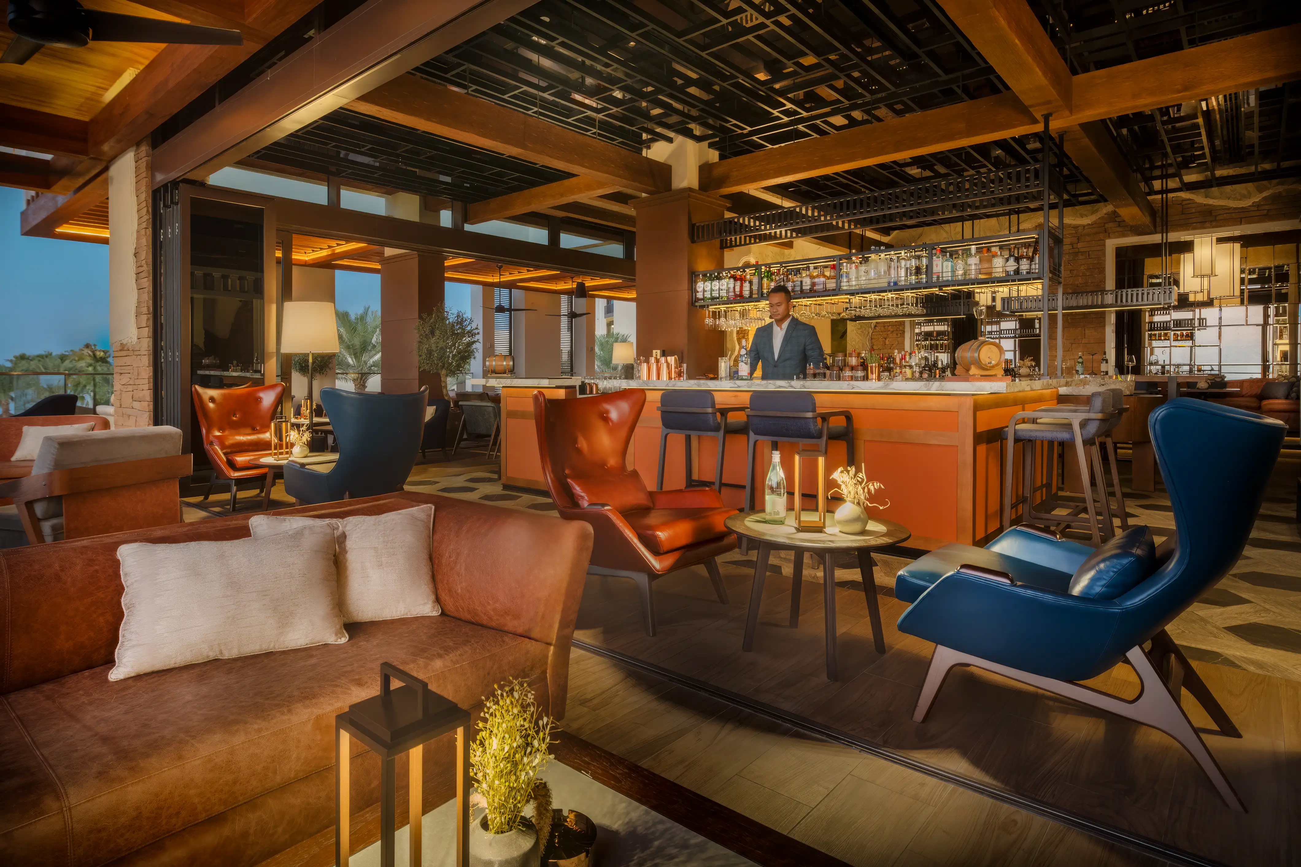 Bar lounge with leather armchairs, a central bar counter and timber beams overhead at Essenza Bar, Mandarin Oriental, Muscat