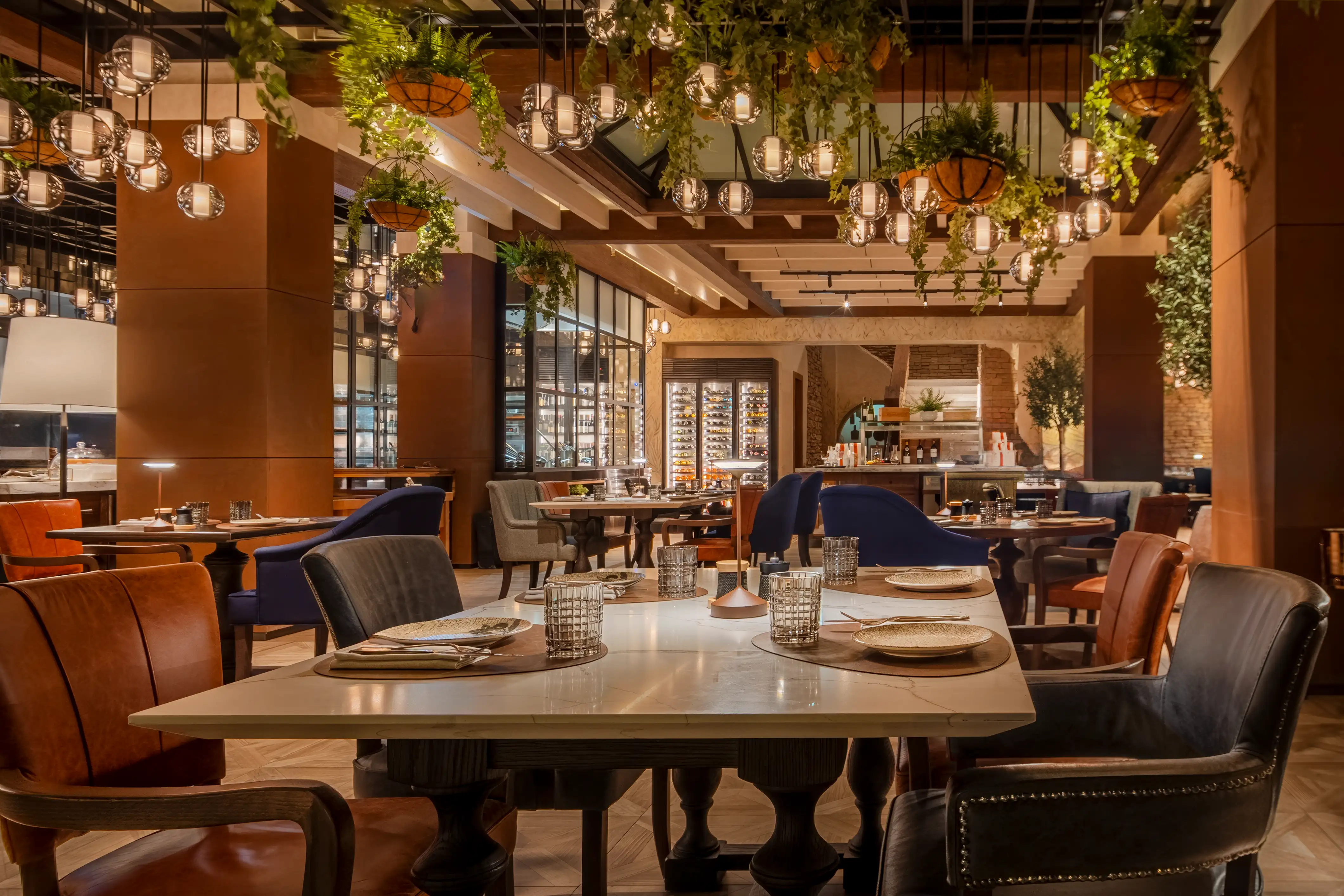 Dining room with leather chairs, hanging planters and globe pendants, with a glass-fronted wine display beyond, at Essenza, Mandarin Oriental, Muscat