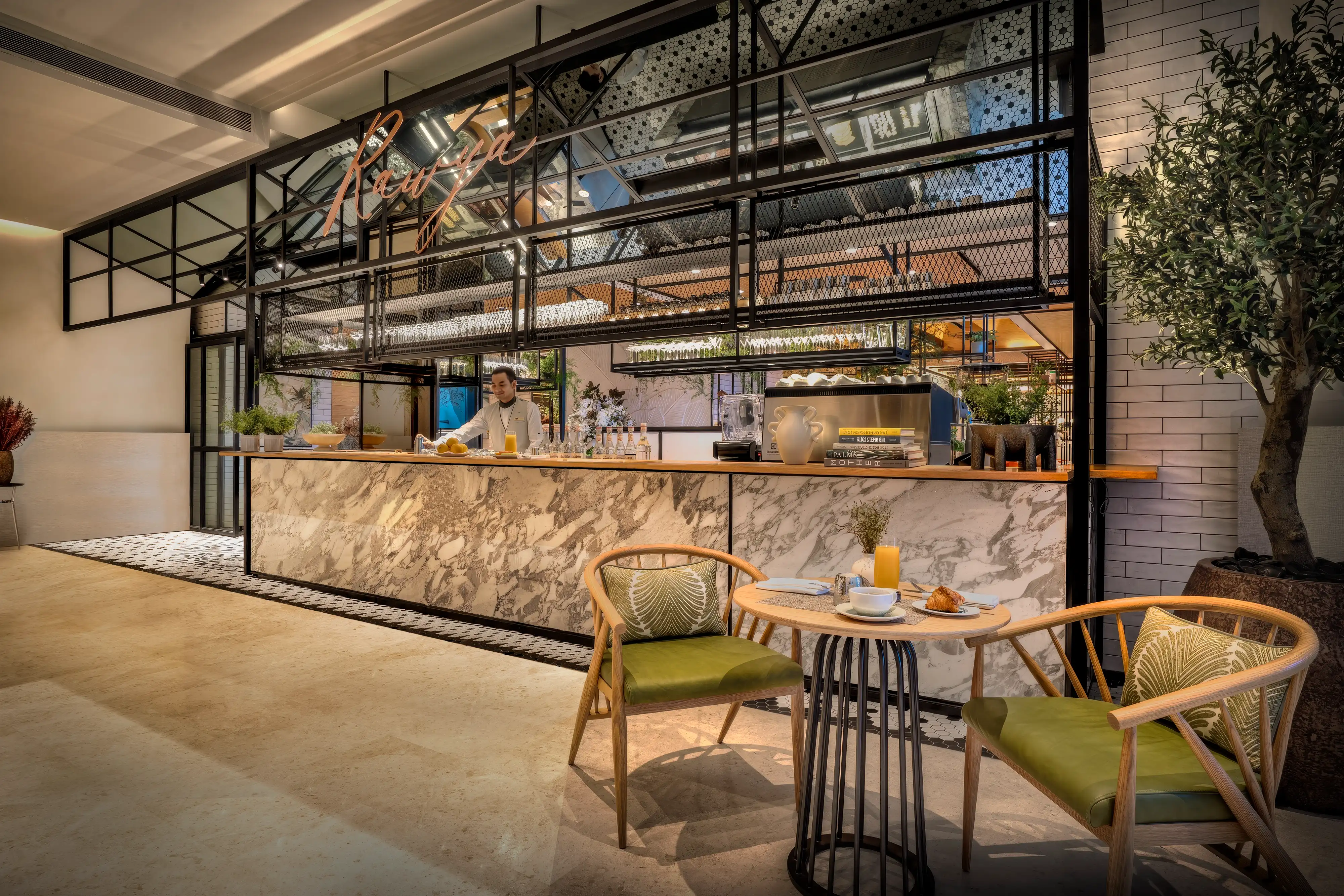 Juice bar and bakery counter at Rawya, Mandarin Oriental, Muscat, with marble cladding, a black steel and glass frame and green-cushioned armchairs
