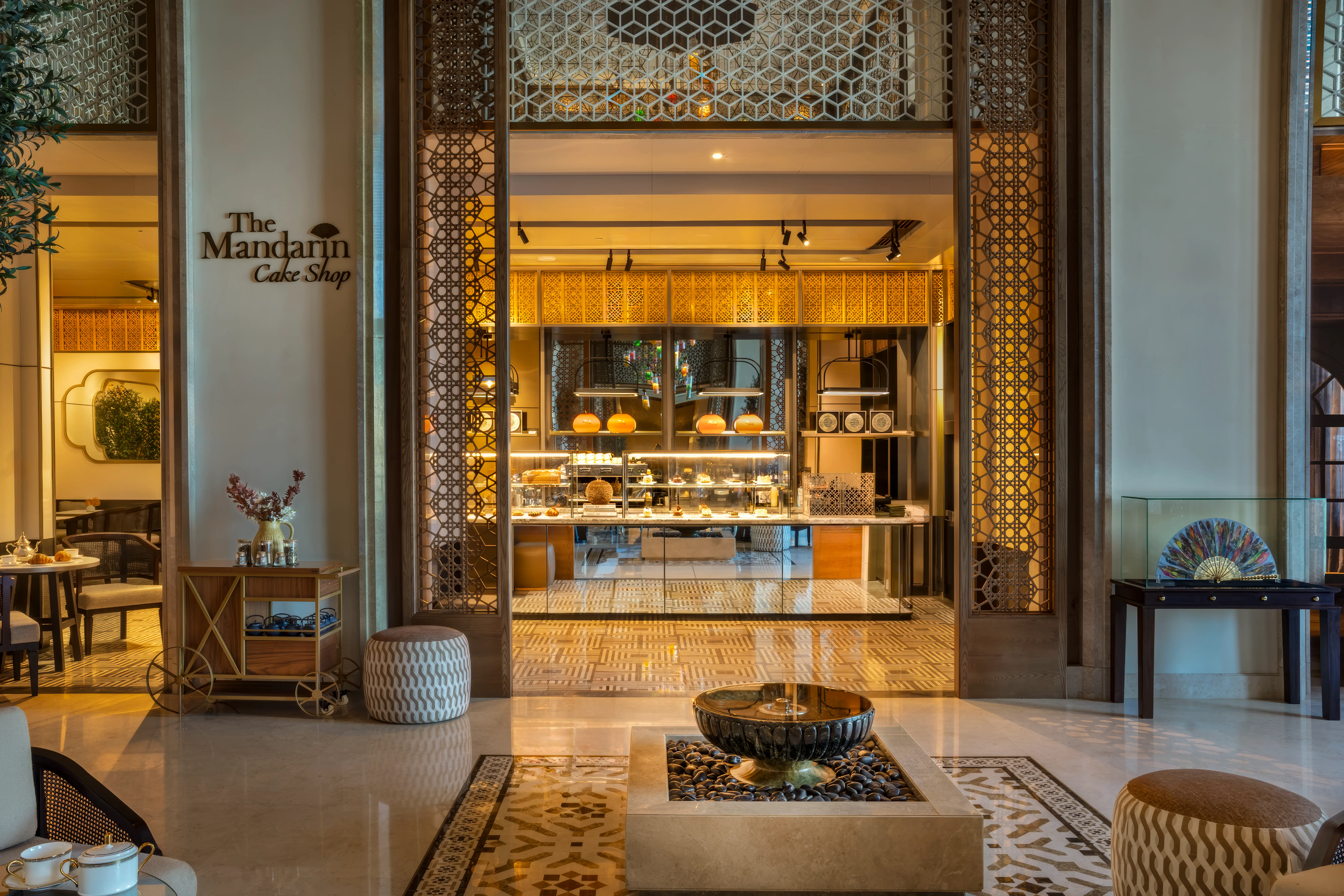 Entrance to The Mandarin Cake Shop with carved lattice screens, a pastry counter and a lobby fountain at Mandarin Oriental, Muscat