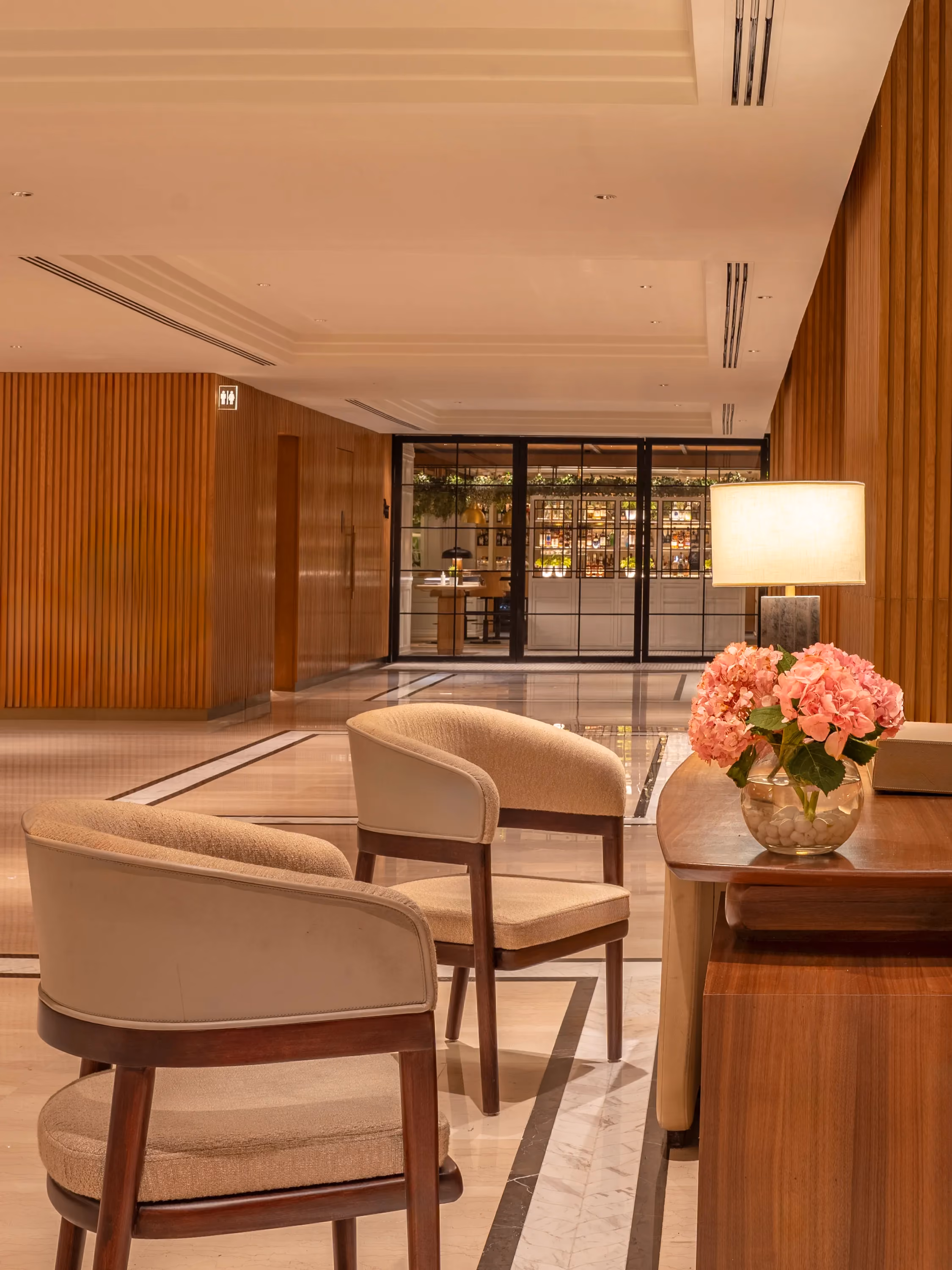 Upholstered armchairs beside fluted timber panelling and black-framed glass doors in the lobby at Trident, Nariman Point