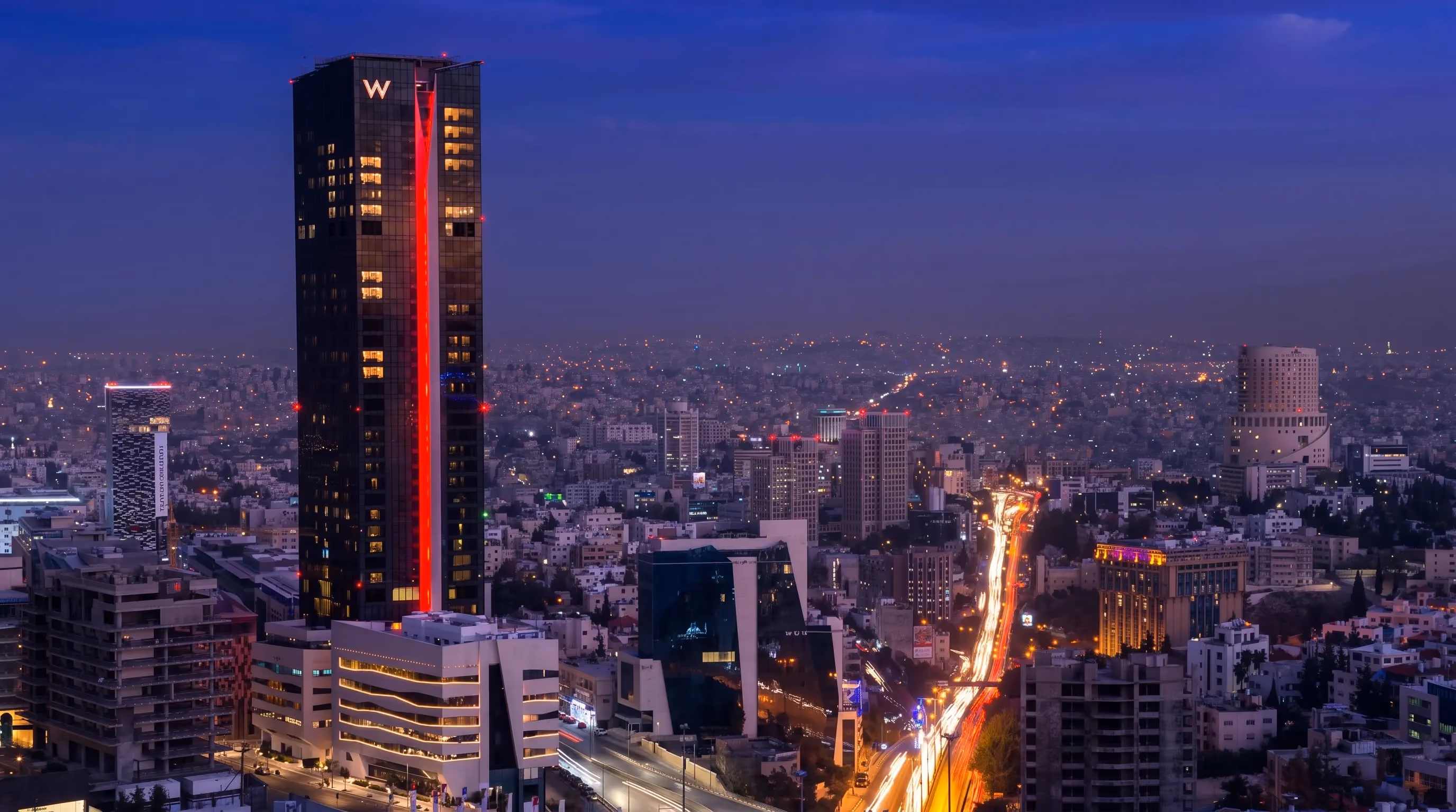W Amman tower at night with a vertical red light line, rising above the Amman skyline