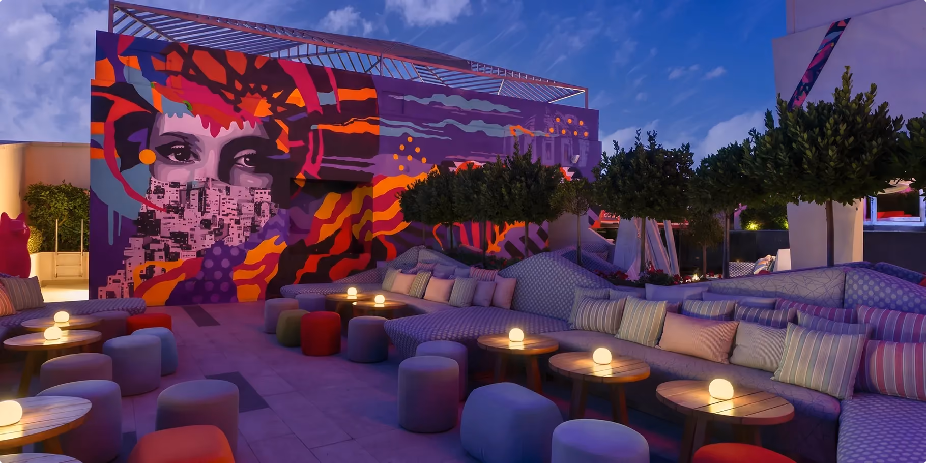 WET Deck at W Amman at night with terraced lounge seating, pouffes and a large mural of a face