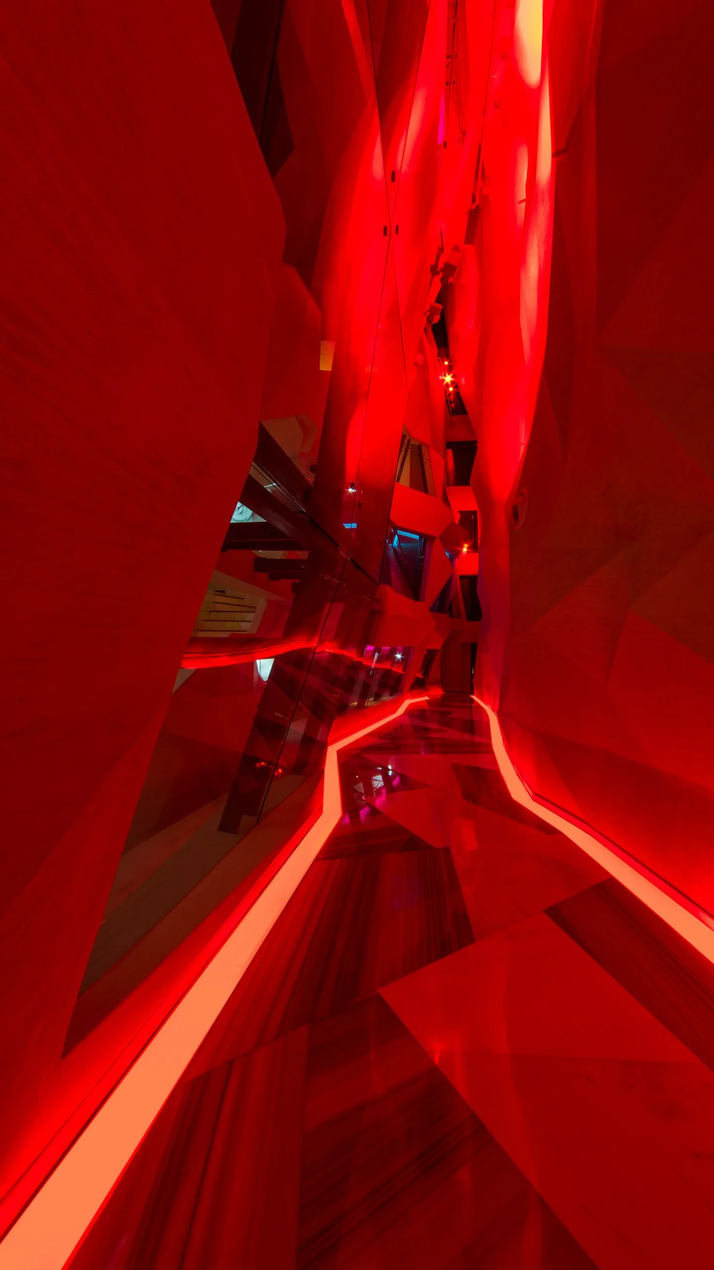 W Amman Canyon Walk arrival, a faceted red lit passage with lines of light along the floor, inspired by the Siq at Petra
