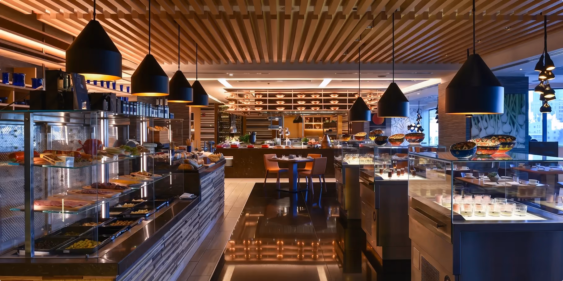 Mesh buffet stations at W Amman under a slatted timber ceiling with clusters of black pendant lights