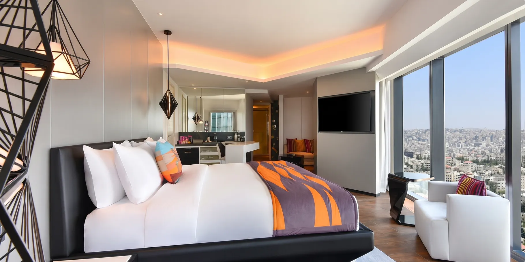 Suite at W Amman with an orange and purple patterned bed throw, a lattice floor lamp and floor to ceiling windows over Amman