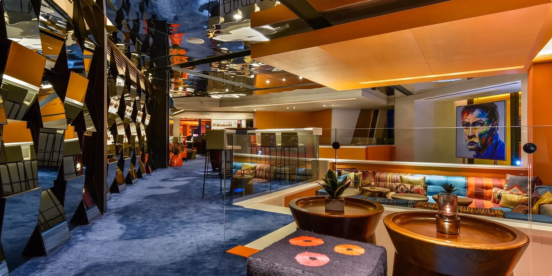 The Living Room lounge at W Amman with faceted mirrored panels, striped banquettes, round side tables and a portrait artwork