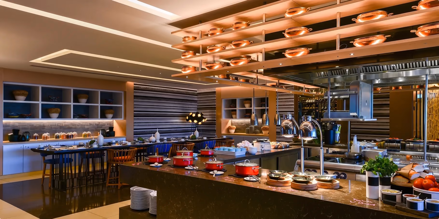 Mesh open kitchen at W Amman with copper pans on open shelving above the show stations and striped wall panels