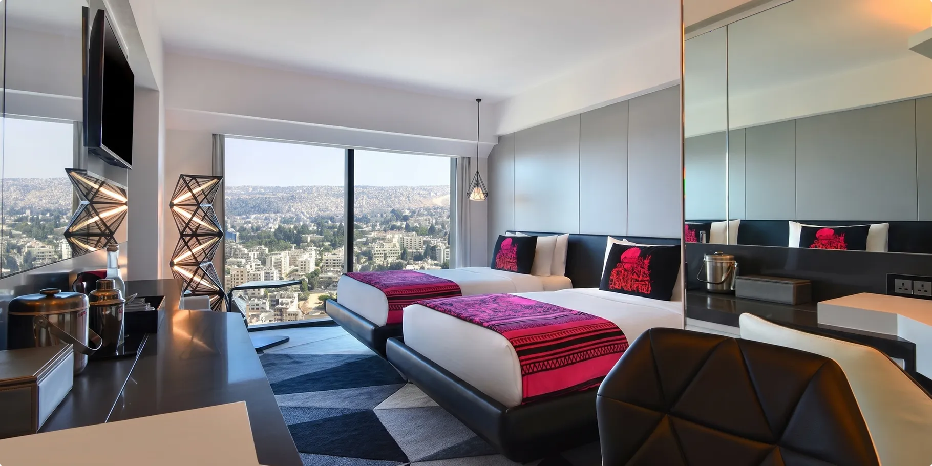 Twin guestroom at W Amman with magenta bed runners, lattice floor lamps and floor to ceiling windows over the city