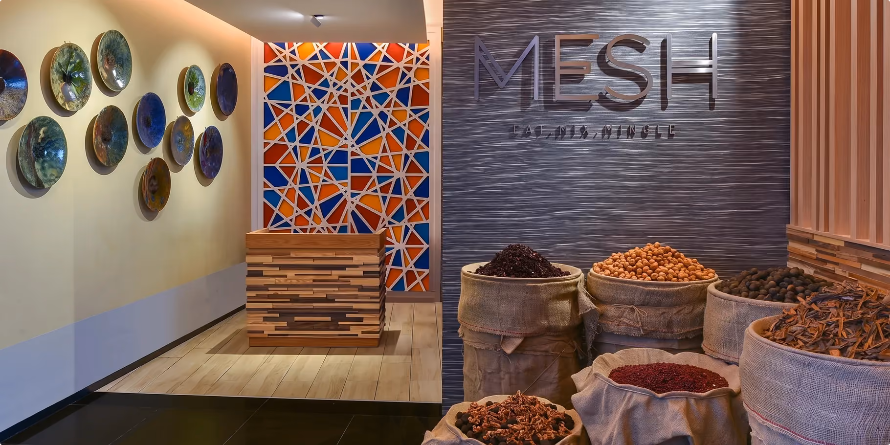 Mesh entrance at W Amman with sacks of spices, a geometric stained glass style panel and decorative plates on the wall