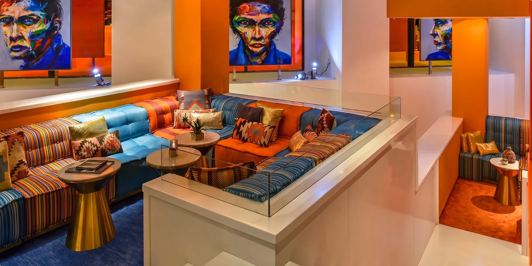 The Living Room at W Amman with multicoloured striped banquettes, scatter cushions and portrait artworks on orange walls