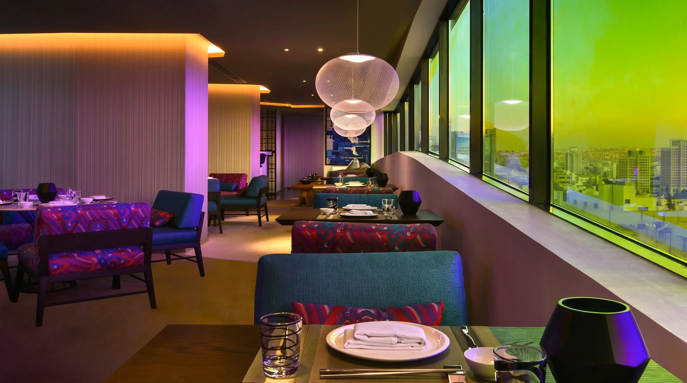 Enso dining room at W Amman with patterned purple banquettes, globe pendant lights and floor to ceiling windows over the city