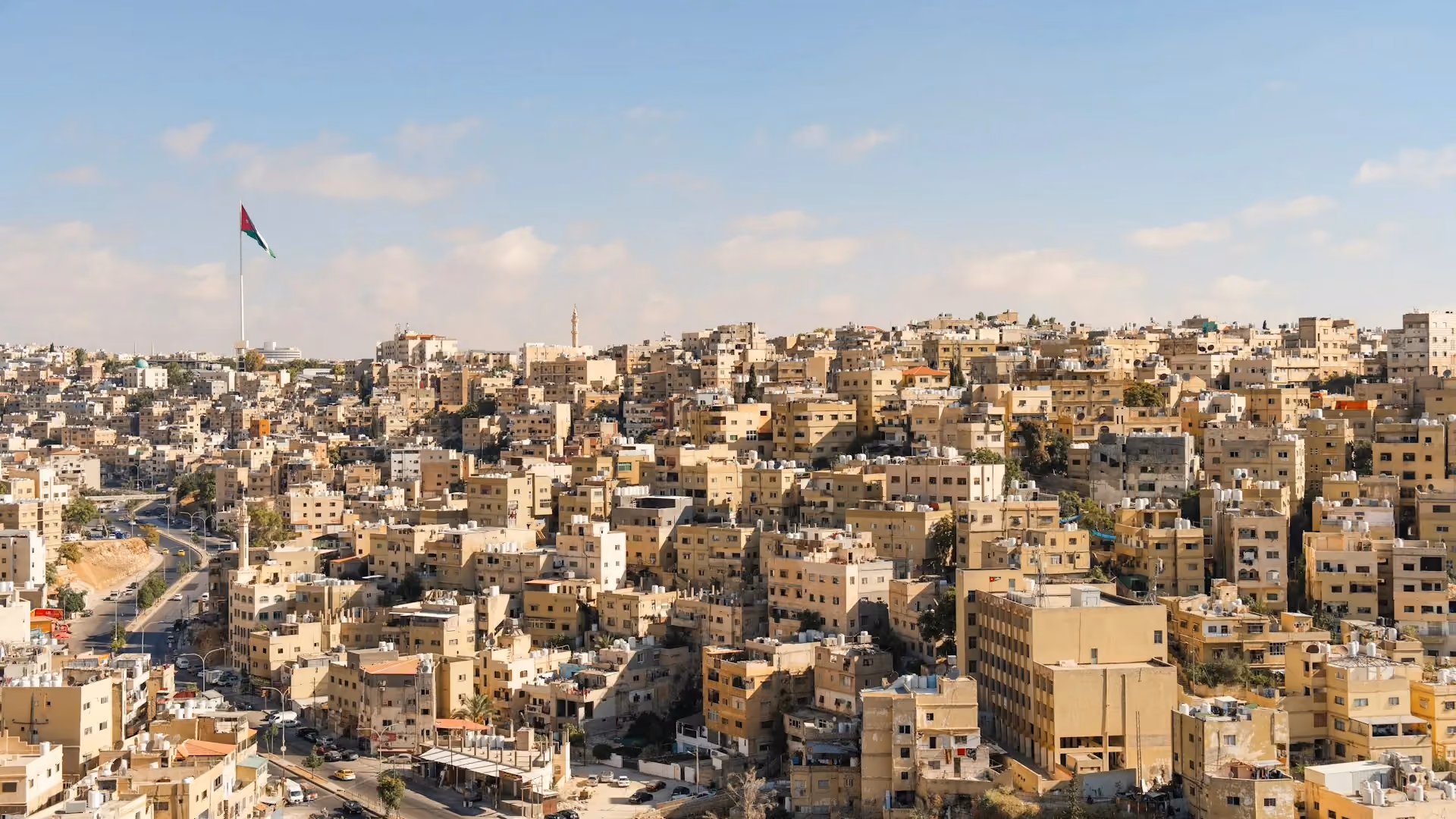 Amman cityscape of white and beige limestone buildings across the hills, with the Jordanian flag