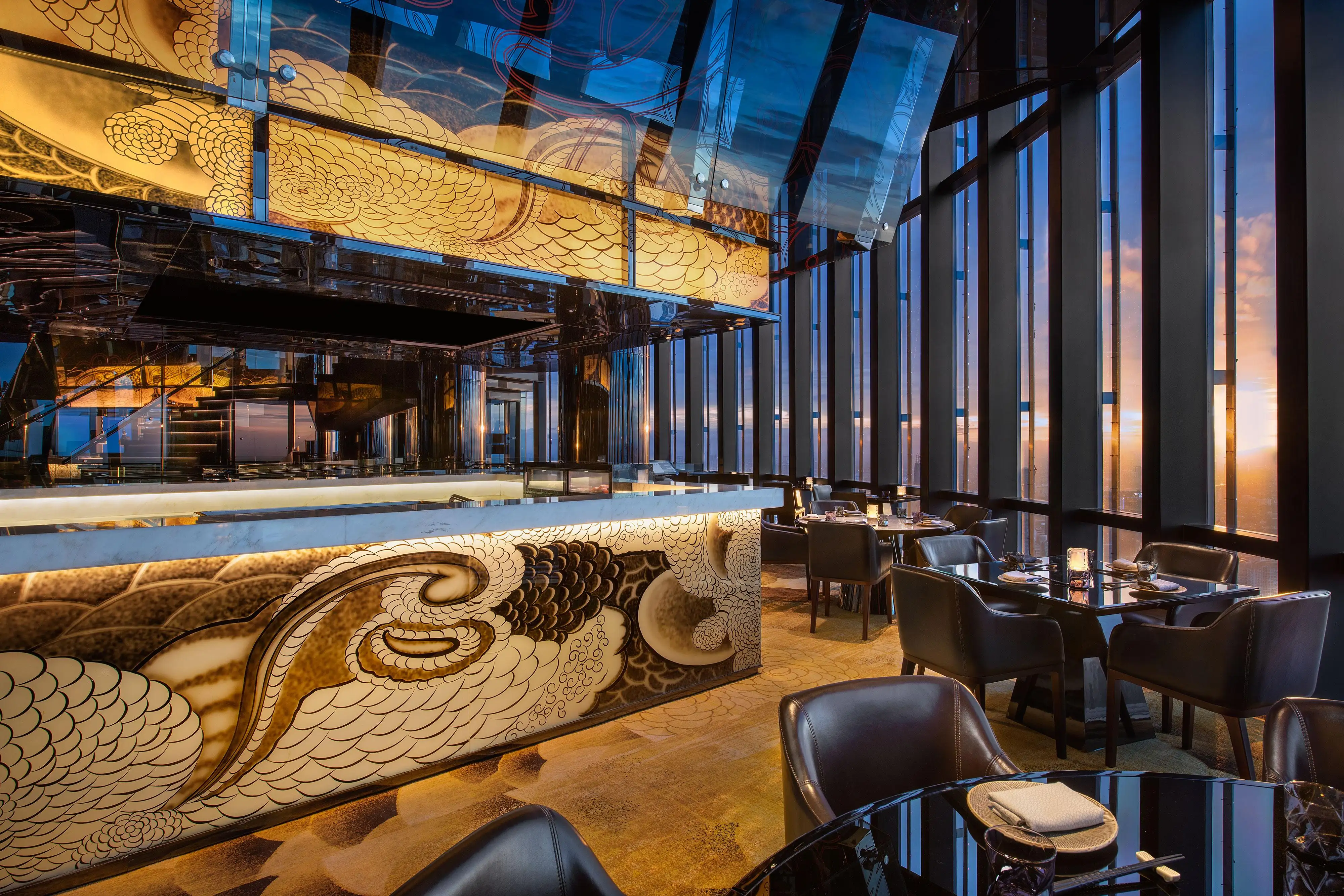 Level 68 main dining at Henshin, The Westin Jakarta, with leather chairs along floor-to-ceiling windows and backlit amber panels above the kitchen