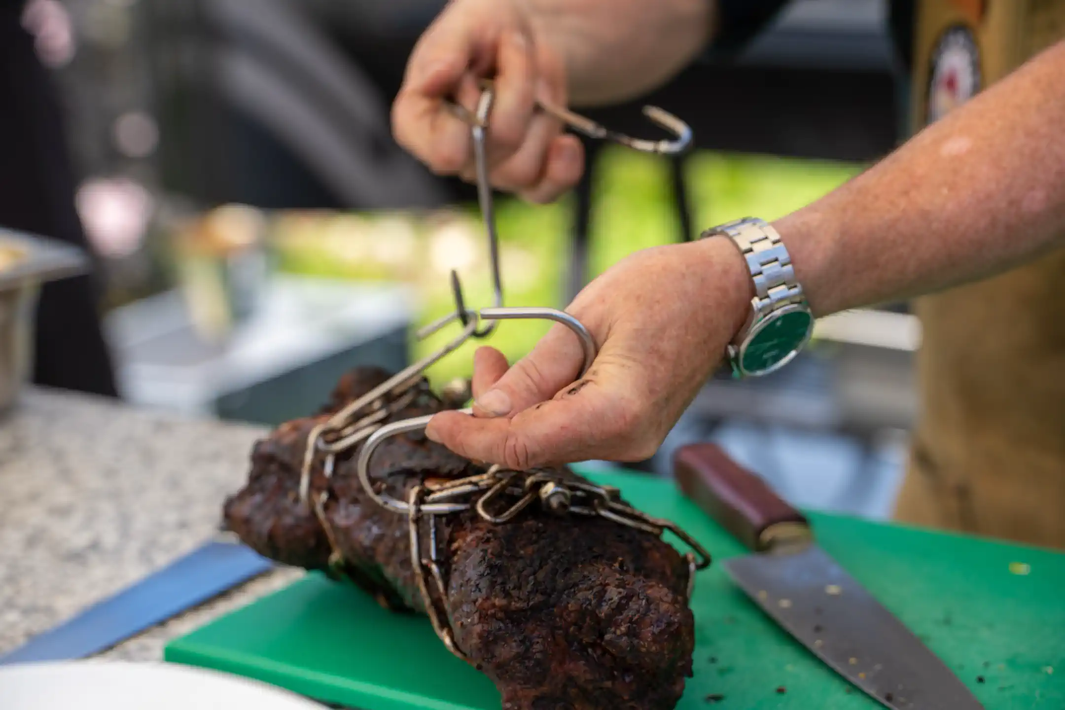 Frisch gegarter Braten vom offenen Feuer wird mit der Zange vorbereitet