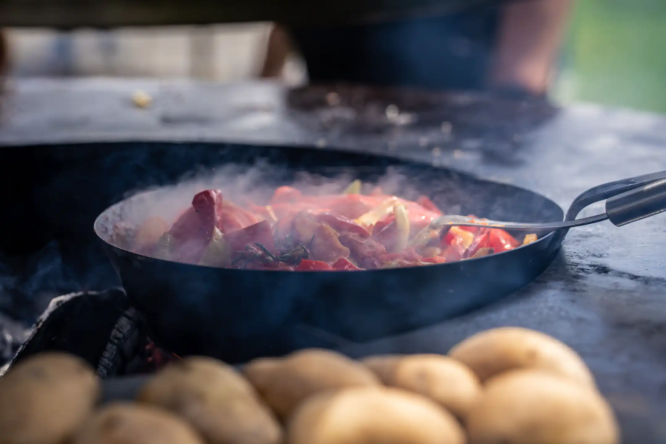 Pfanne mit Fleisch und Paprika auf der heißen Feuerplatte, davor Kartoffeln