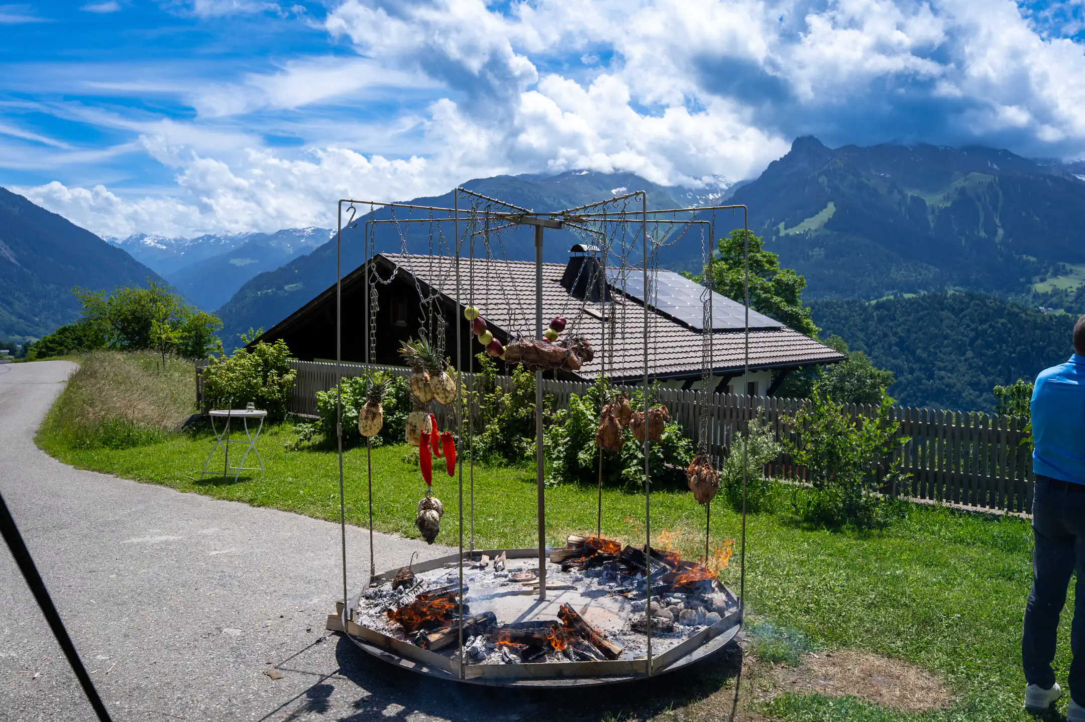 Großes Grillgestell mit Fleisch über der Glut vor Bergkulisse