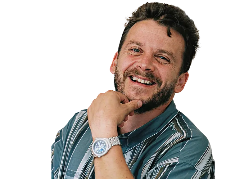 Homme souriant avec barbe, vêtu d'une chemise rayée verte et blanche, portant une montre argentée.