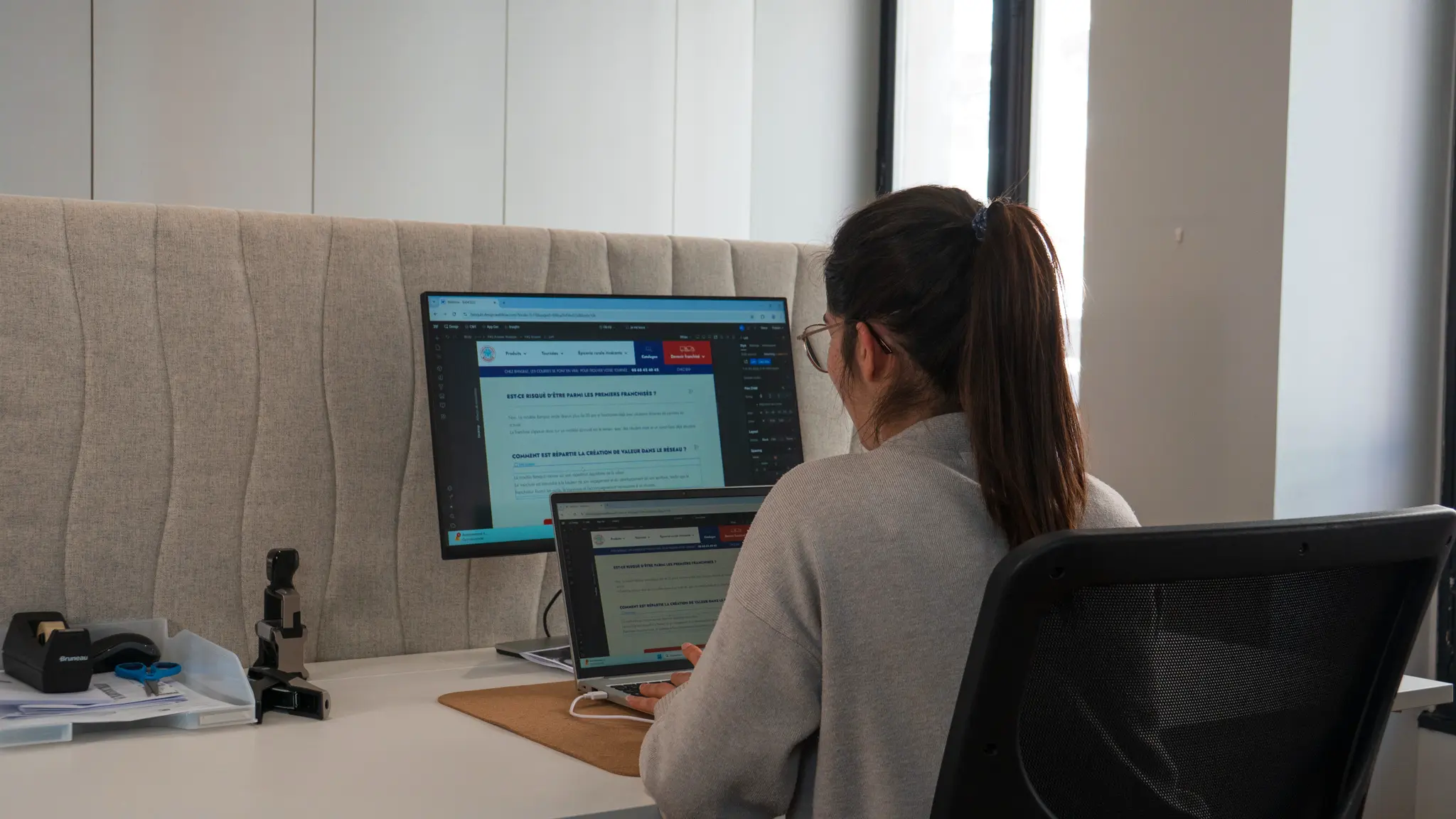 Personne assise à un bureau travaillant sur un ordinateur portable avec un écran d'ordinateur externe affichant du texte en français.