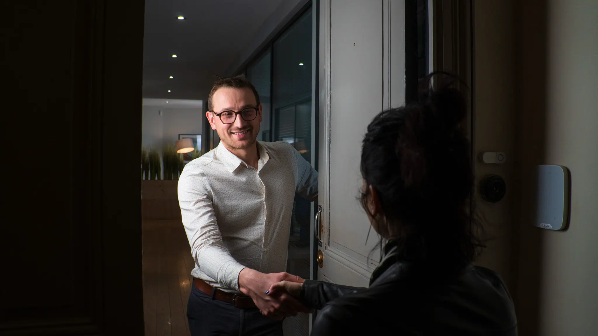 Un homme souriant serre la main d'une femme à l'entrée d'une porte ouverte.
