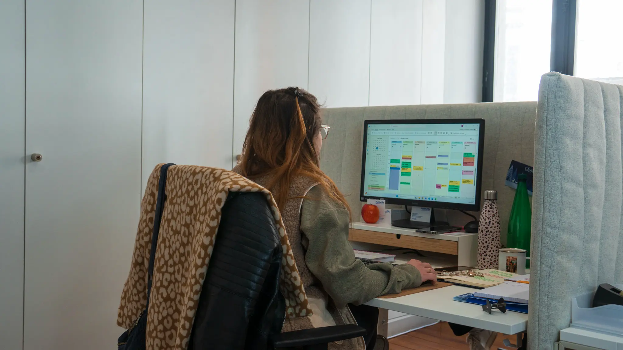 Personne assise à un bureau regardant un écran d'ordinateur affichant un calendrier numérique coloré.