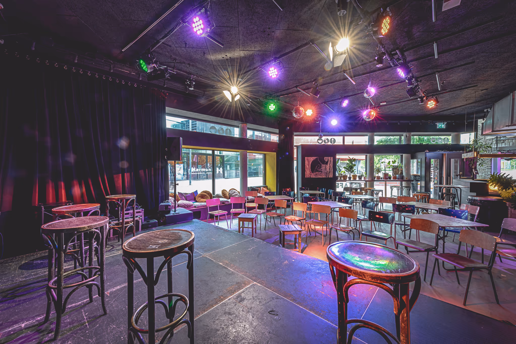 Neushoorn Café vanaf het podium gezien, met stoeltjes en tafels, een vensterbank met kussens en veel ramen met planten