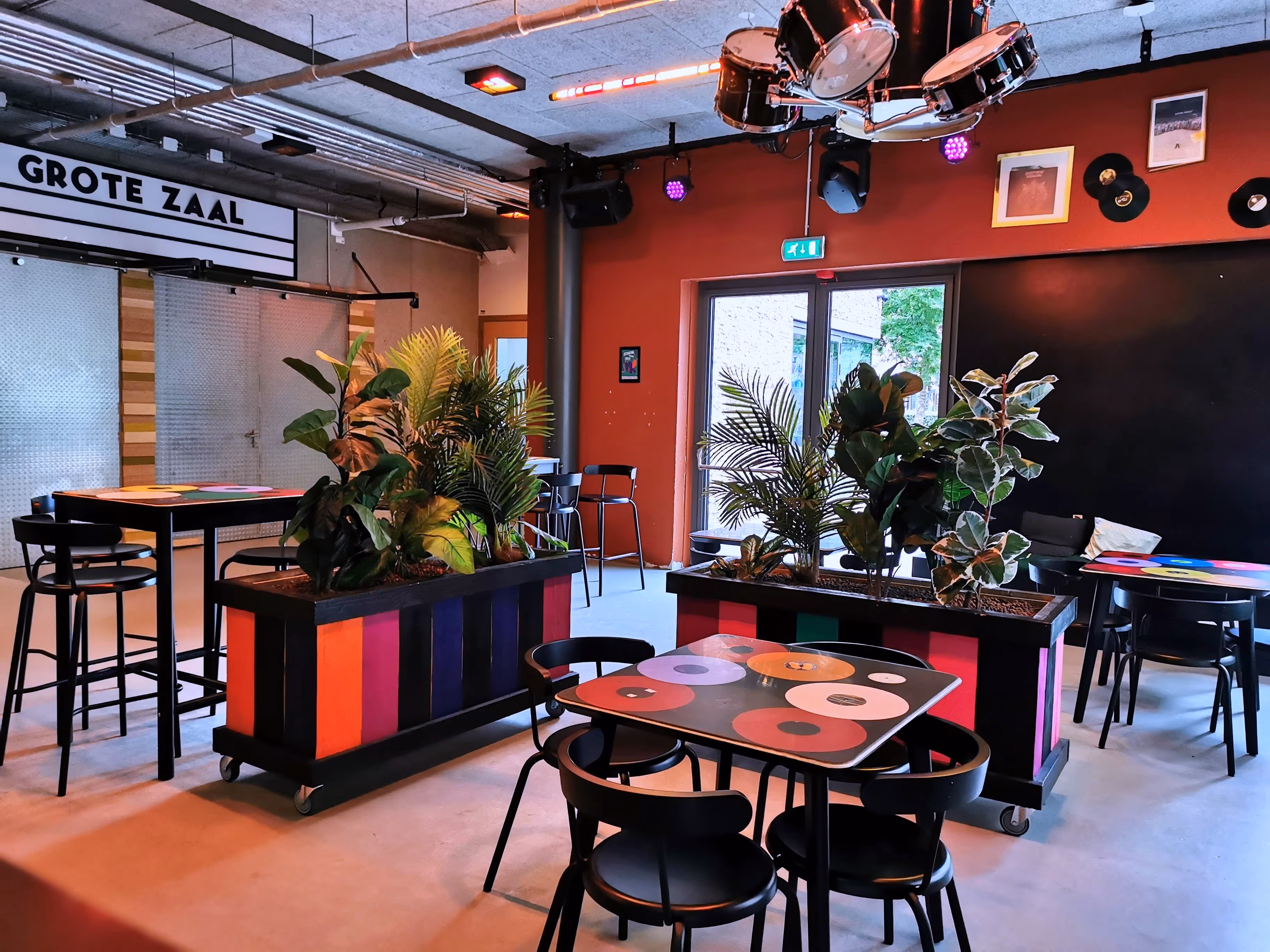 Sfeervol hoekje bij de Grote Zaal met taefels die gedecoreerd zijn met elpees, een drumstellamp en plantenbakken met vorlijke kleuren.