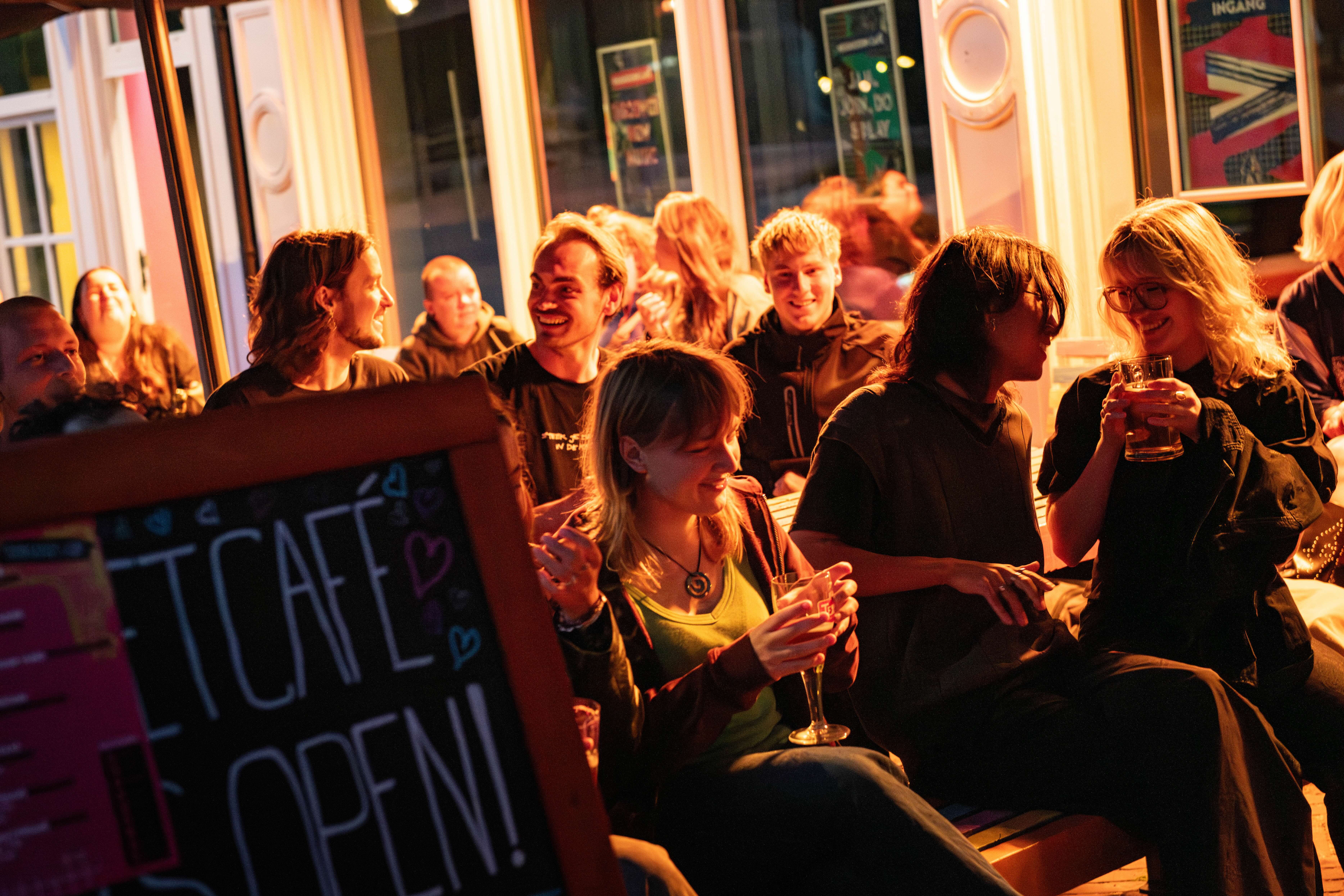 Neushoorn Café vanaf het podium gezien, met stoeltjes en tafels, een vensterbank met kussens en veel ramen met planten