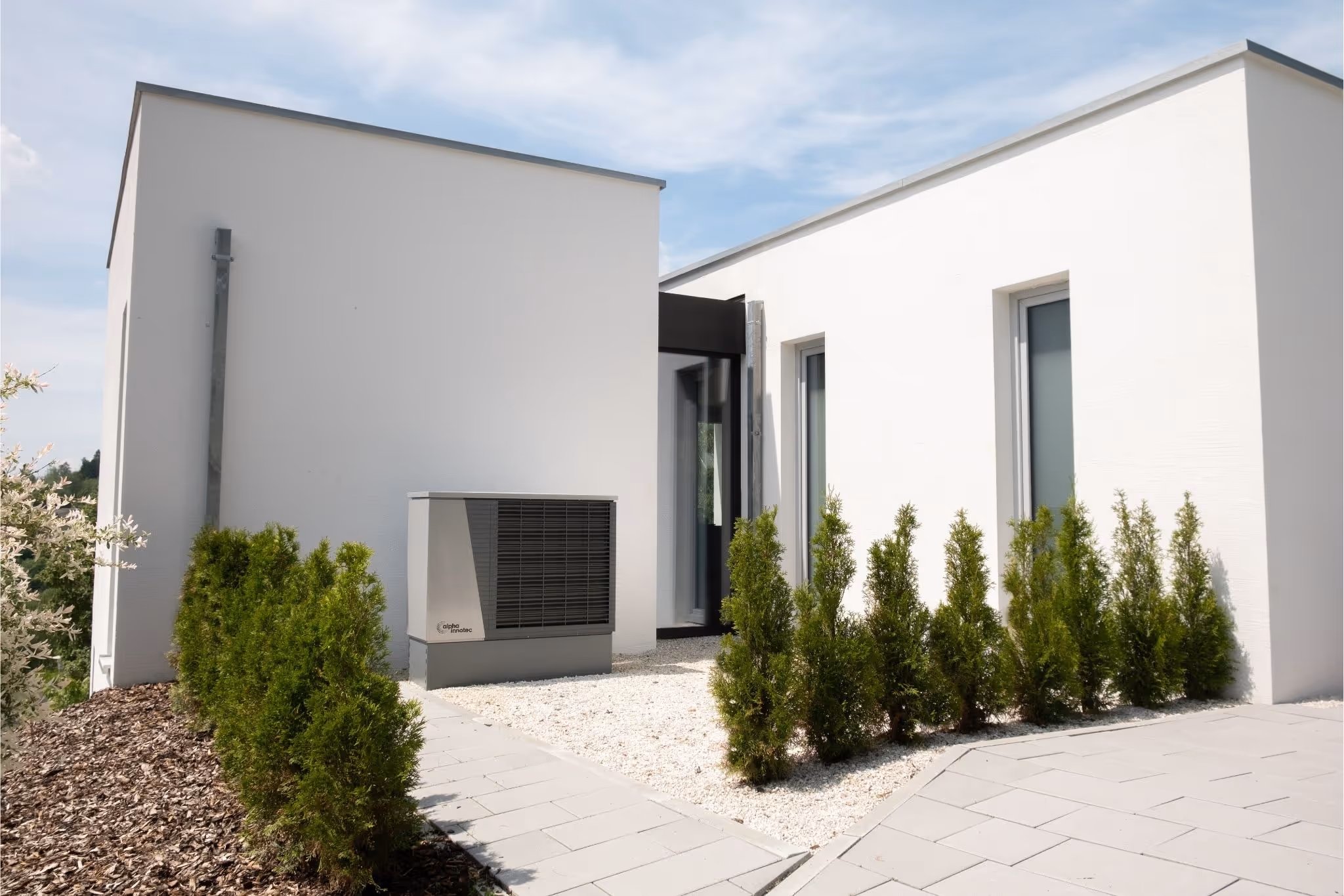 Wärmepumpe von Alpha Innotec vor modernem Haus mit Begrünung