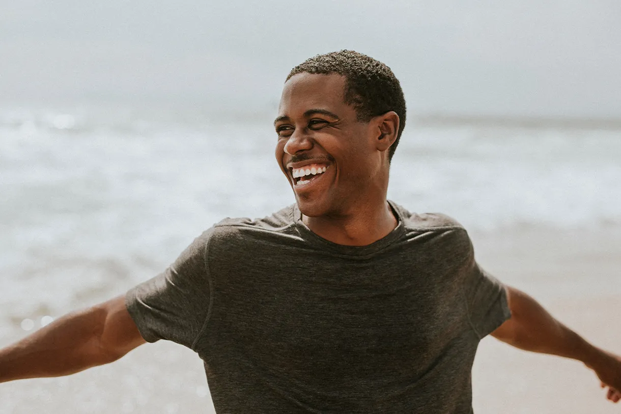 African American man outside at the beach smiles with healthy, white, straight teeth after Invisalign in San Francisco