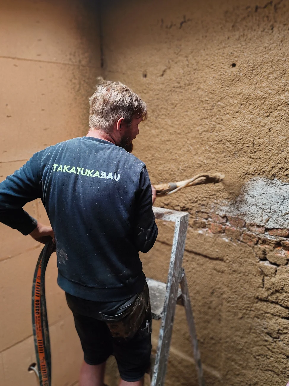 Takatukabau-Handwerker verputzt Innenwand mit Lehm, nachhaltige Sanierung in Freiburg.