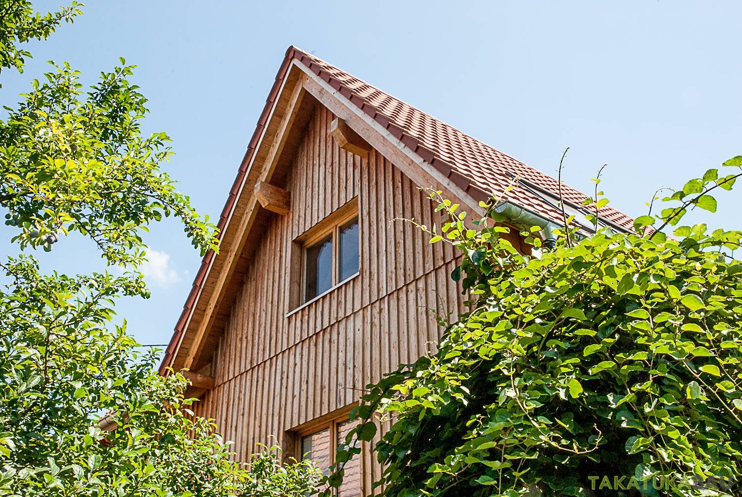 Sanierte Holzfassade und rotes Ziegeldach eines Einfamilienhauses von Takatukabau in Freiburg, eingerahmt von grünem Garten.