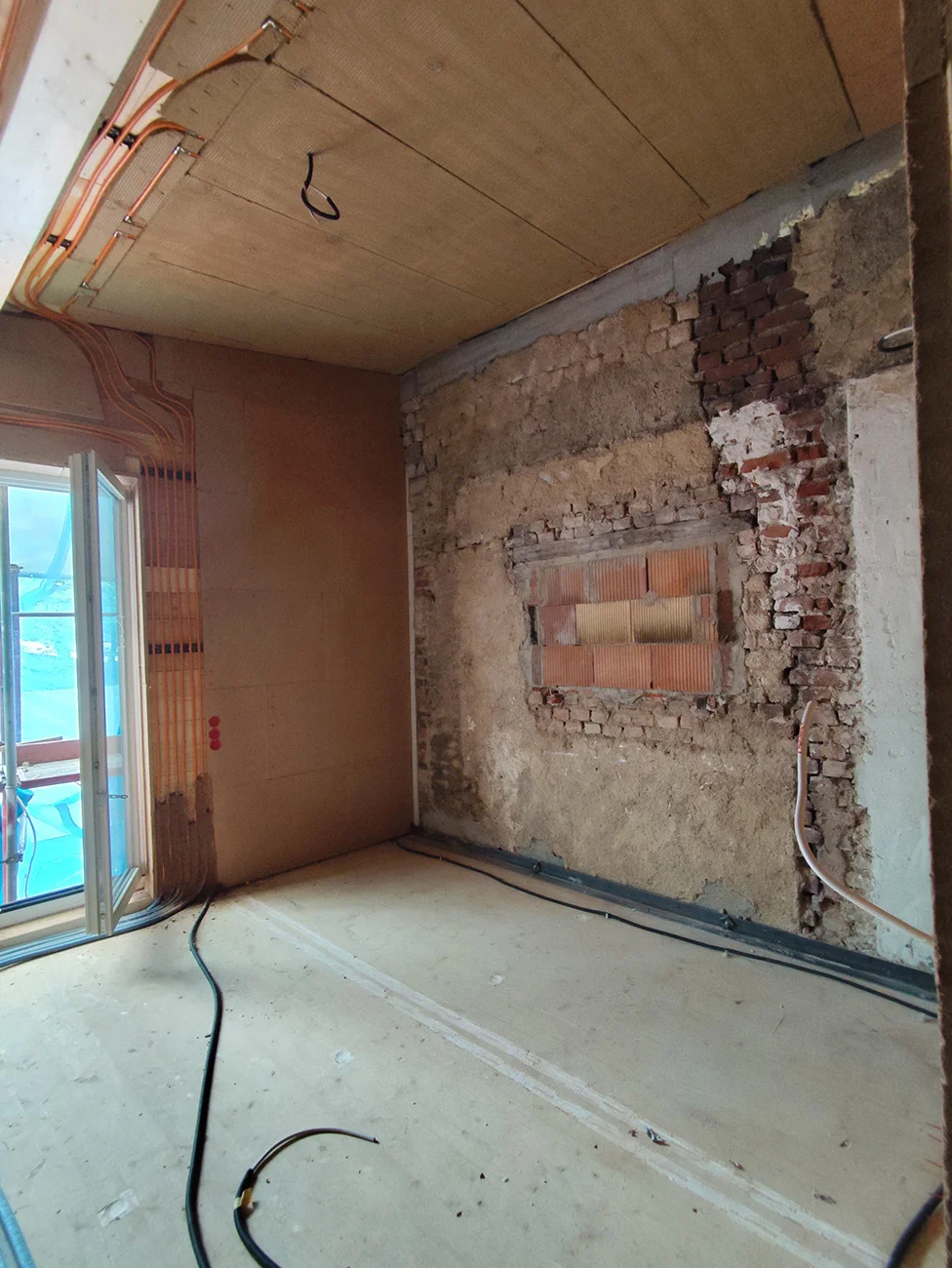 Innenraumsanierung: Rückgebaute Ziegelwand, Holzfaser-Deckenelemente mit Heizschlangen und neue Fensterlaibung, Takatukabau.