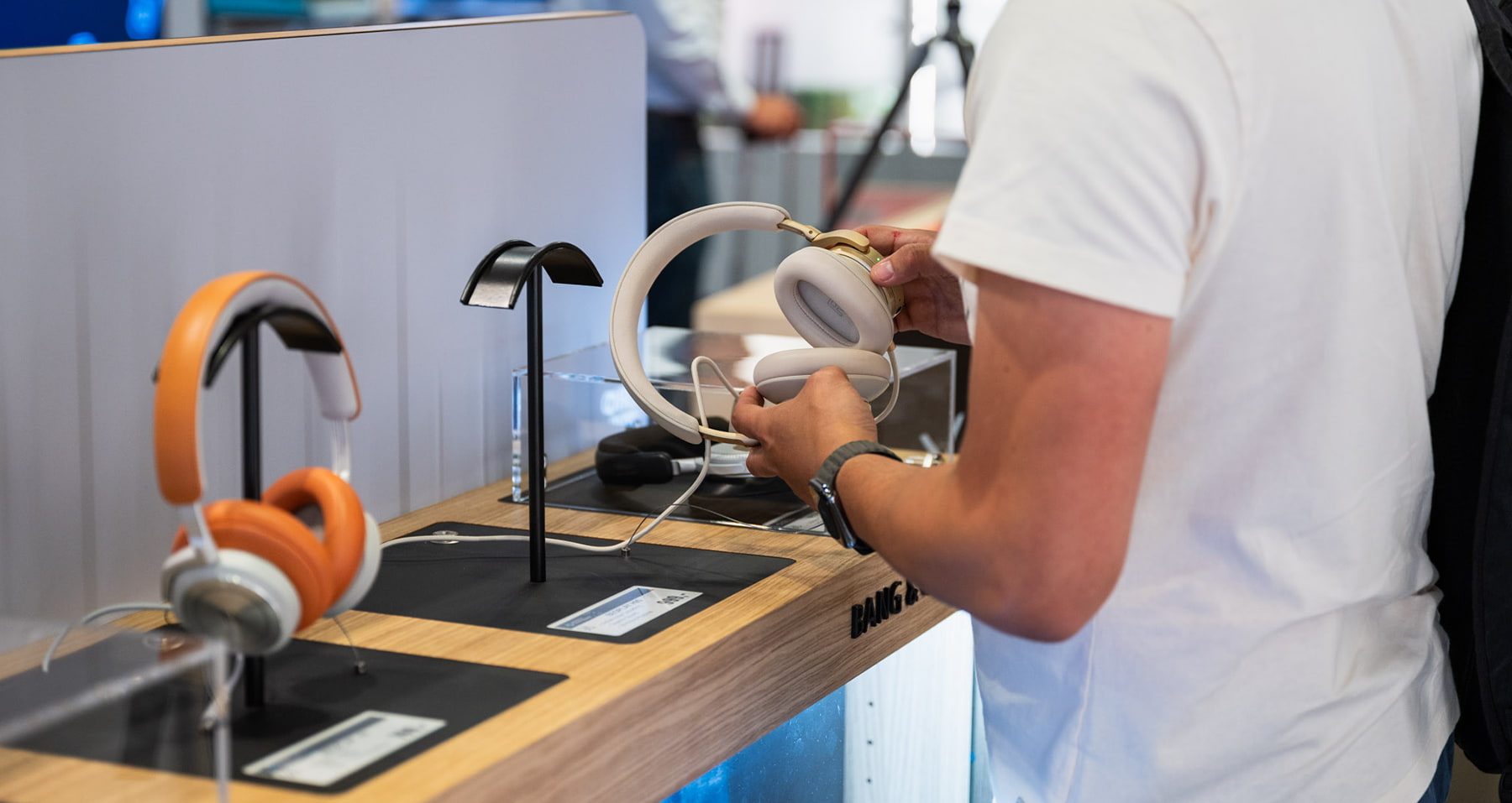 Kunde testet kabellose Over-Ear-Kopfhörer an einer Präsentationsstation im Elektronik-Shop von PAX Airport Shopping.