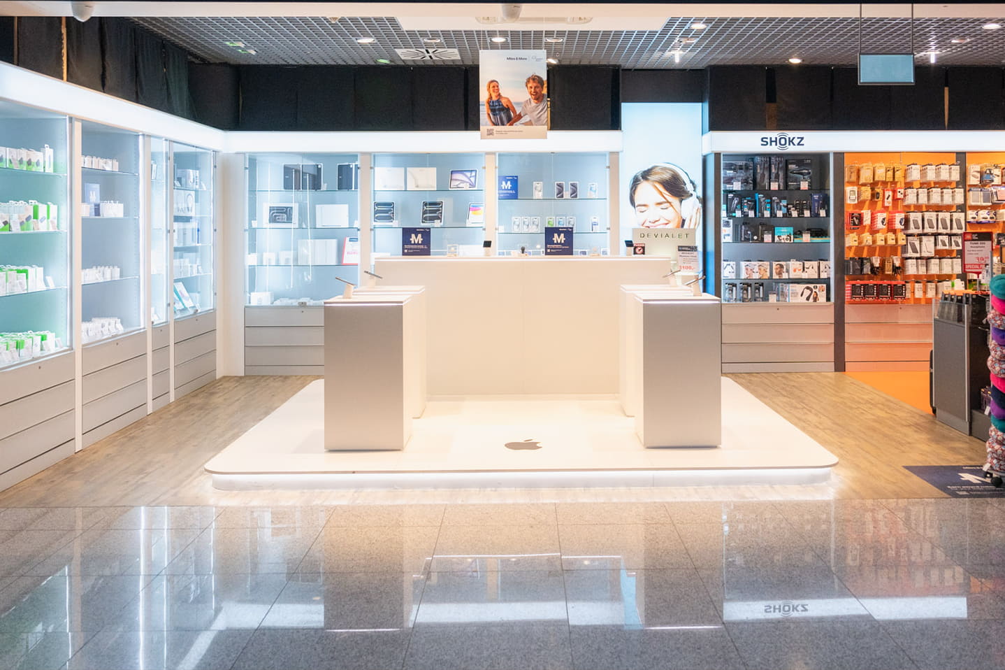„Zentraler Verkaufsbereich eines Elektronik-Shops im Flughafen mit beleuchteten Präsentationsflächen, Vitrinen für Zubehör und geordneten Produktregalen im Hintergrund.