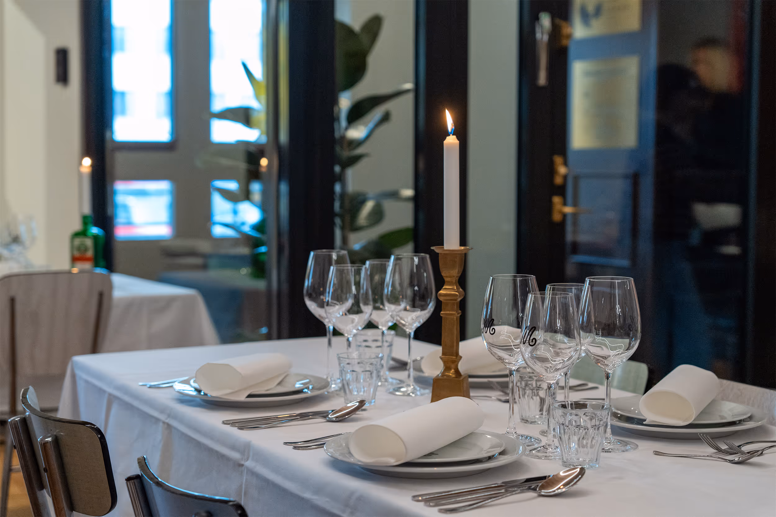 Table set with plates, glasses, cutlery, and a candle at Restaurant Madame.