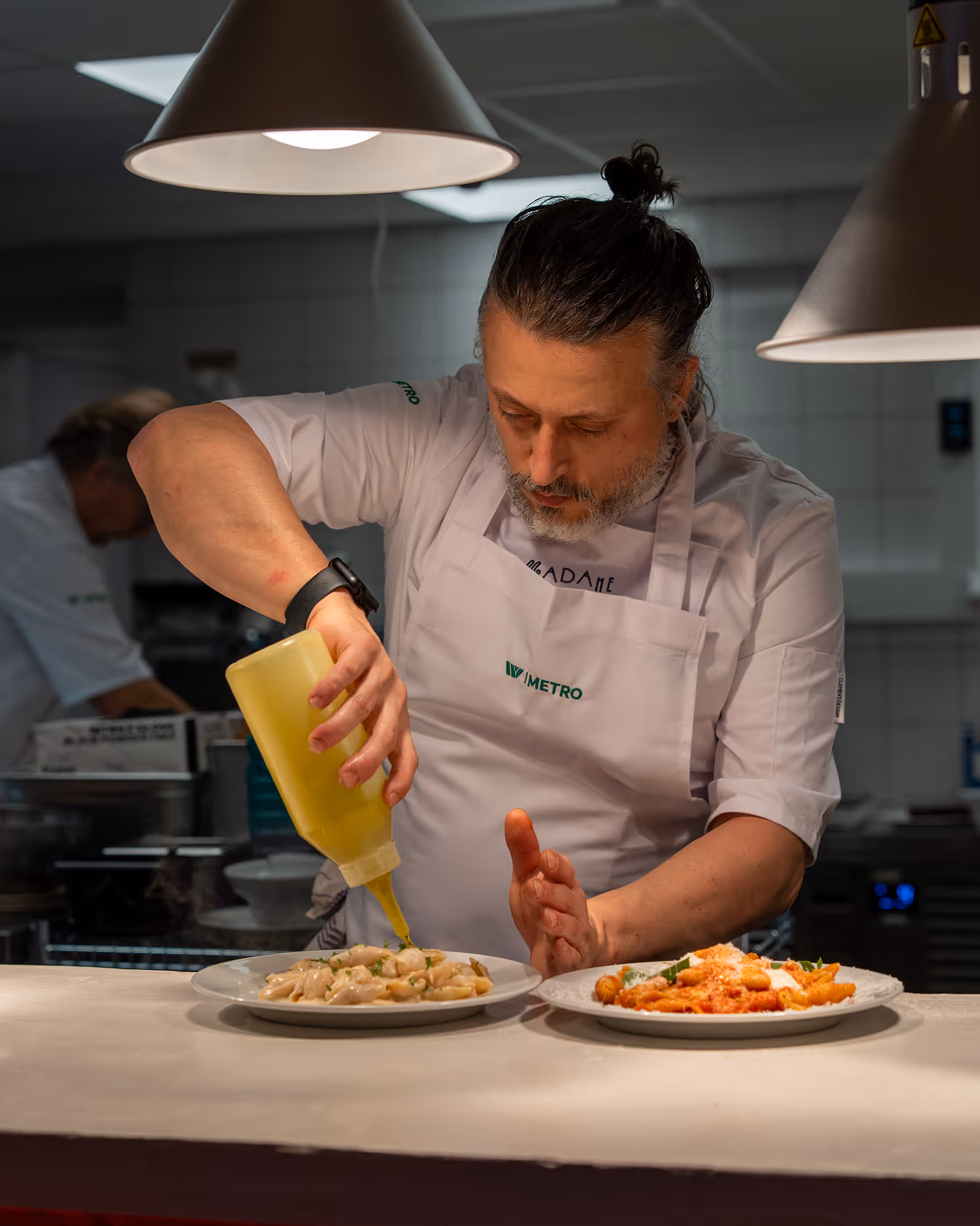 Chef at Restaurant Madame adding sauce to pasta plates in the kitchen.