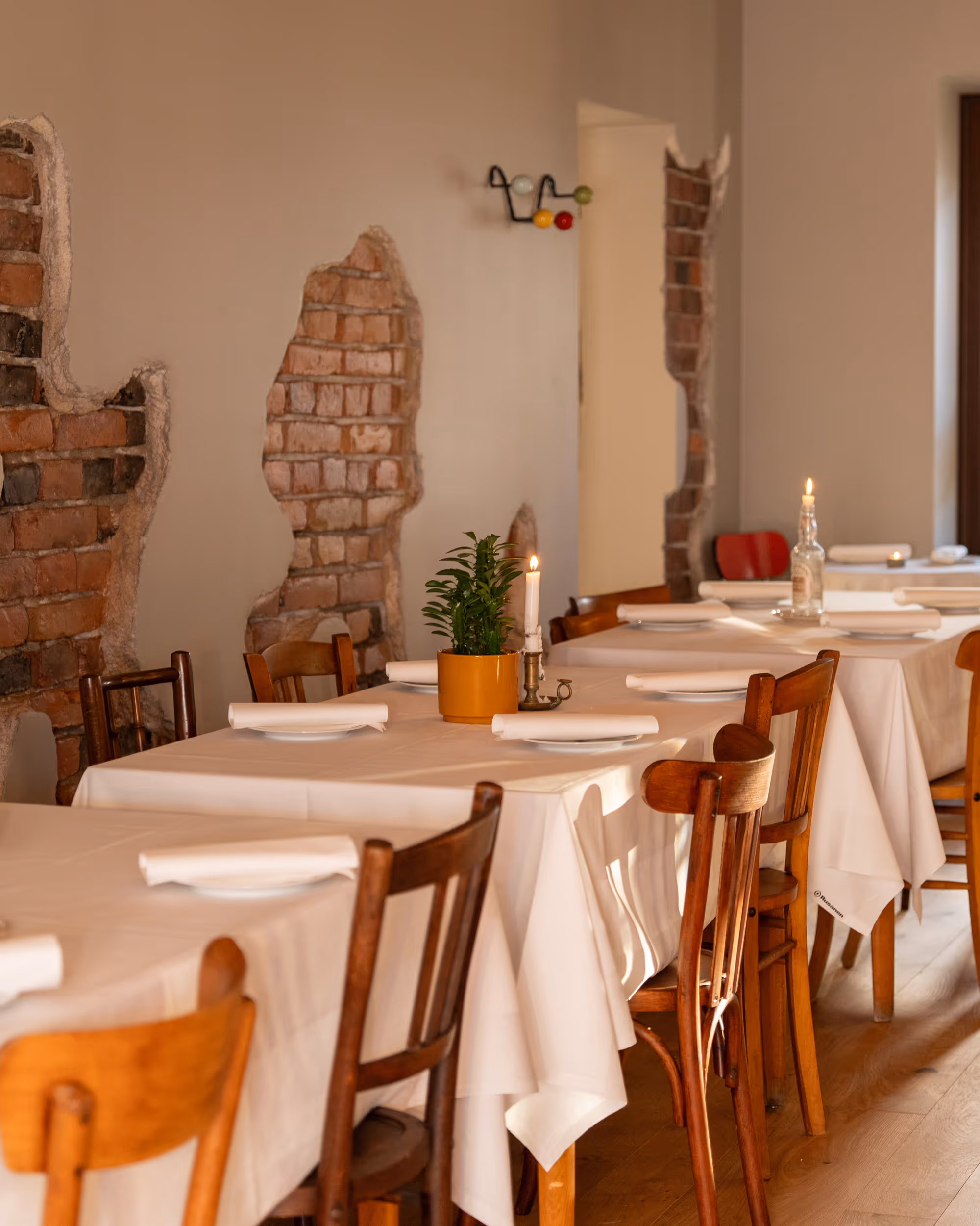 Dining area at Restaurant Madame with wooden chairs, white tablecloths, and exposed brick walls.
