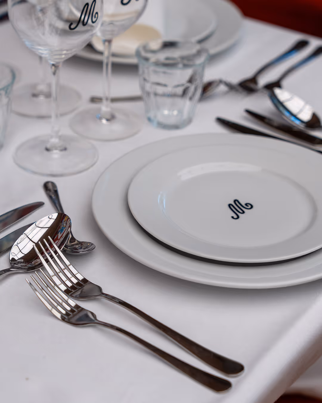 Table setting at Restaurant Madame with plates, cutlery, and wine glasses featuring the Madame logo.