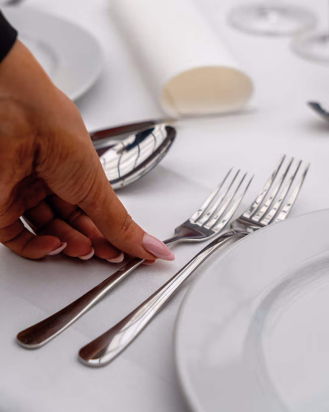 Hand adjusting forks on a neatly set table at Restaurant Madame.