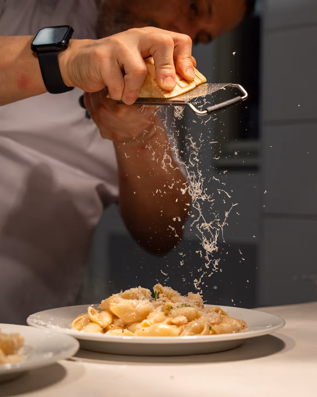 Chef grating cheese over a plate of pasta at Restaurant Madame.